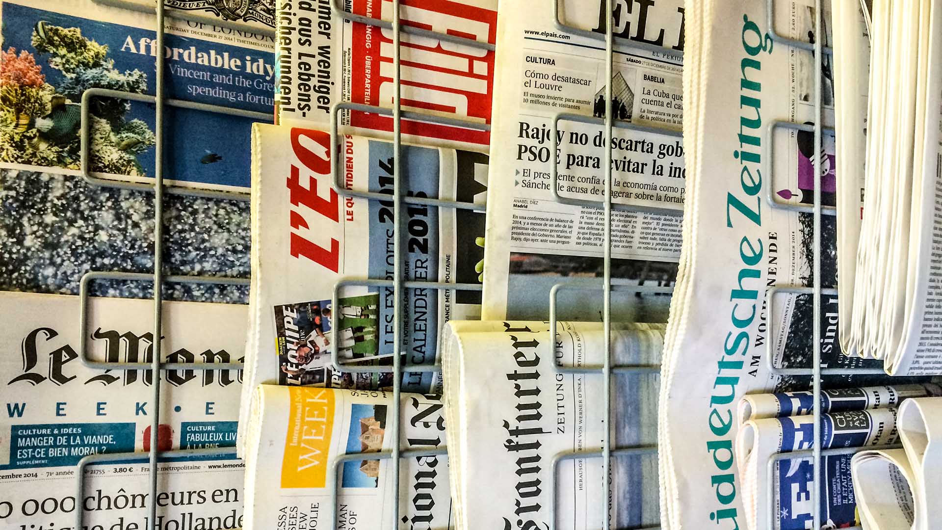 Primer plano de portadas de diferentes periódicos europeos colocados en los soportes de metal.