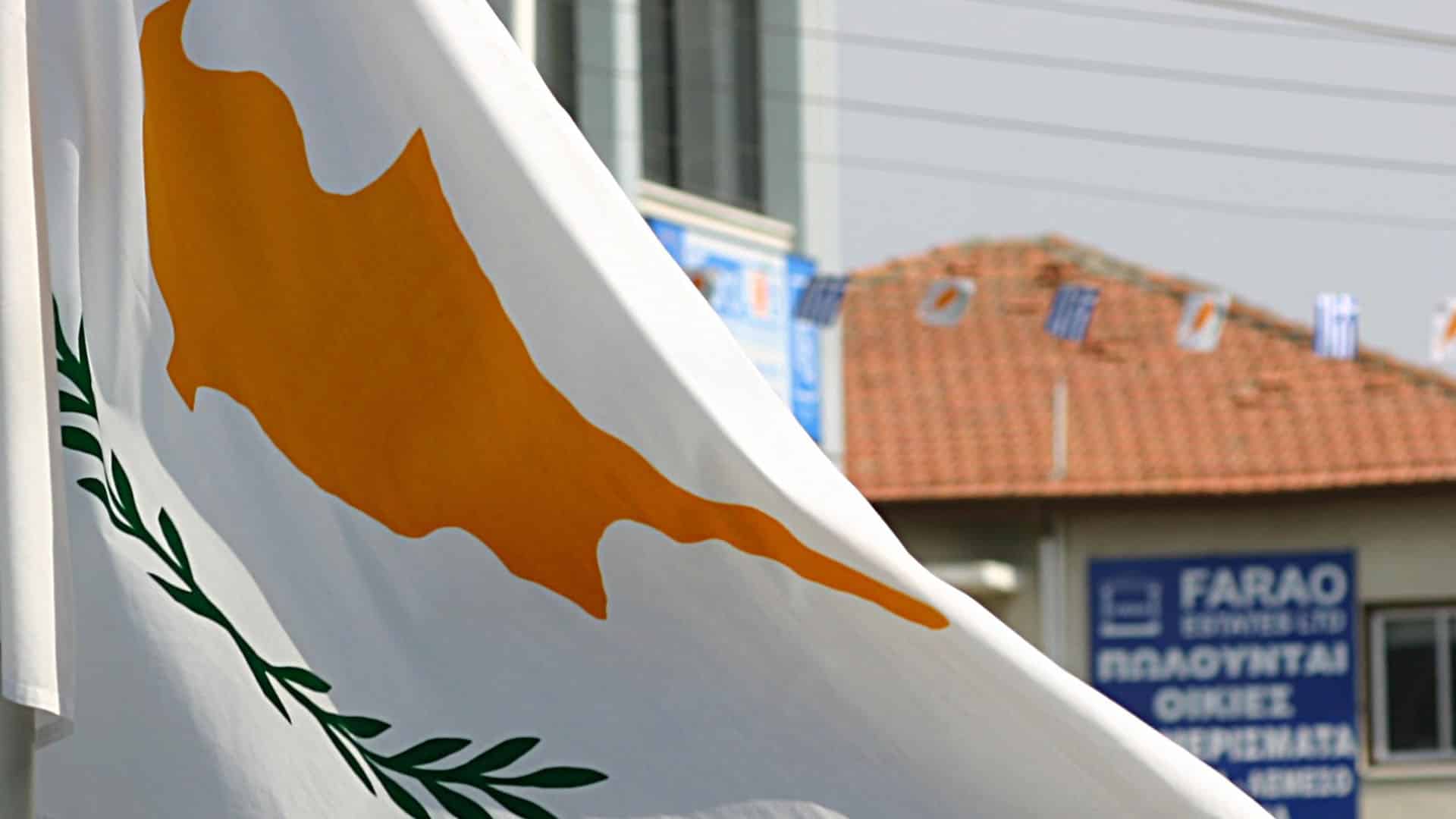 The flag of Cyprus flying in the foreground during an outdoor event.