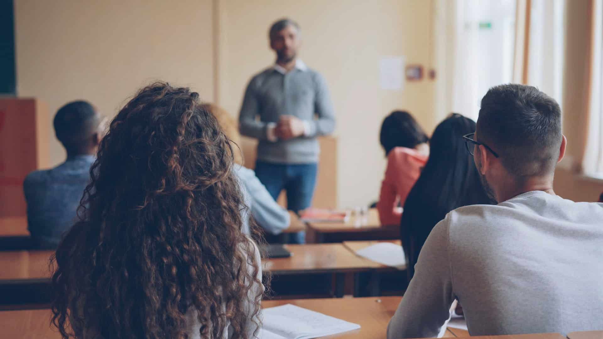 Espaldas de un grupo de jovenes sentados durante un encuentro académico. En primer plano las figuras de una chica y un chico.