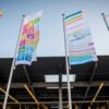 Banderas promocionales con los ODS de la ONU instaladas frente a un edificio moderno de cristal durante el Festival Global de Accíon por el Desarrollo Sostenible.