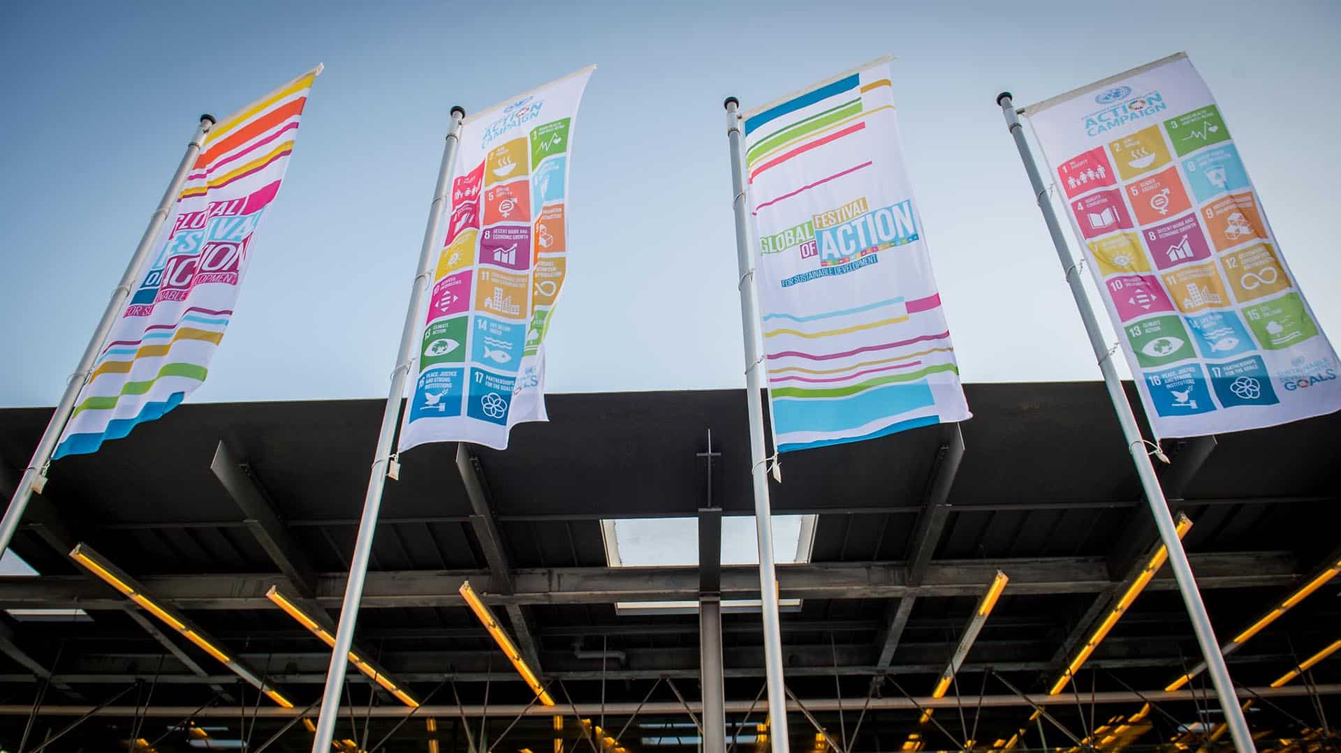 Banderas promocionales con los ODS de la ONU instaladas frente a un edificio moderno de cristal durante el Festival Global de Accíon por el Desarrollo Sostenible.