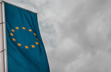 Mundo del mañana. Foto de una bandera de la Unión Europea en formato vertical en un mastil con el cielo nublado y gris