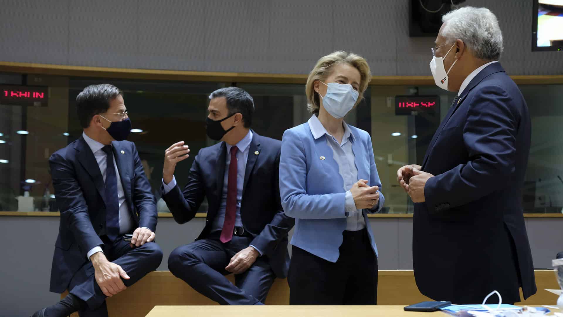 magen del Consejo Europeo extraordinario del 20 de julio de 2020. En el salón del Consejo, en primer plano, Ursula von der Leyen (presidenta de la Comisión Europea) conversa con António Costa (primer ministro de Portugal) frente a una de las mesas con un móvil y mascarillas. Al fondo, Mark Rutte (primer ministro de Países Bajos) y Pedro Sánchez (presidente del Gobierno de España) conversan reclinados en otra mesa de madera. Todos tienen mascarillas.