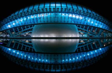 Foto del edificio L’Hemisferic, diseñado por Santiago Calatrava con analogía de un ojo, de noche en la Ciudad de las Artes y las Ciencias de Valencia (España). El edificio está iluminado con luces blancas con filtros azules, dando una idea futurista y distópica.