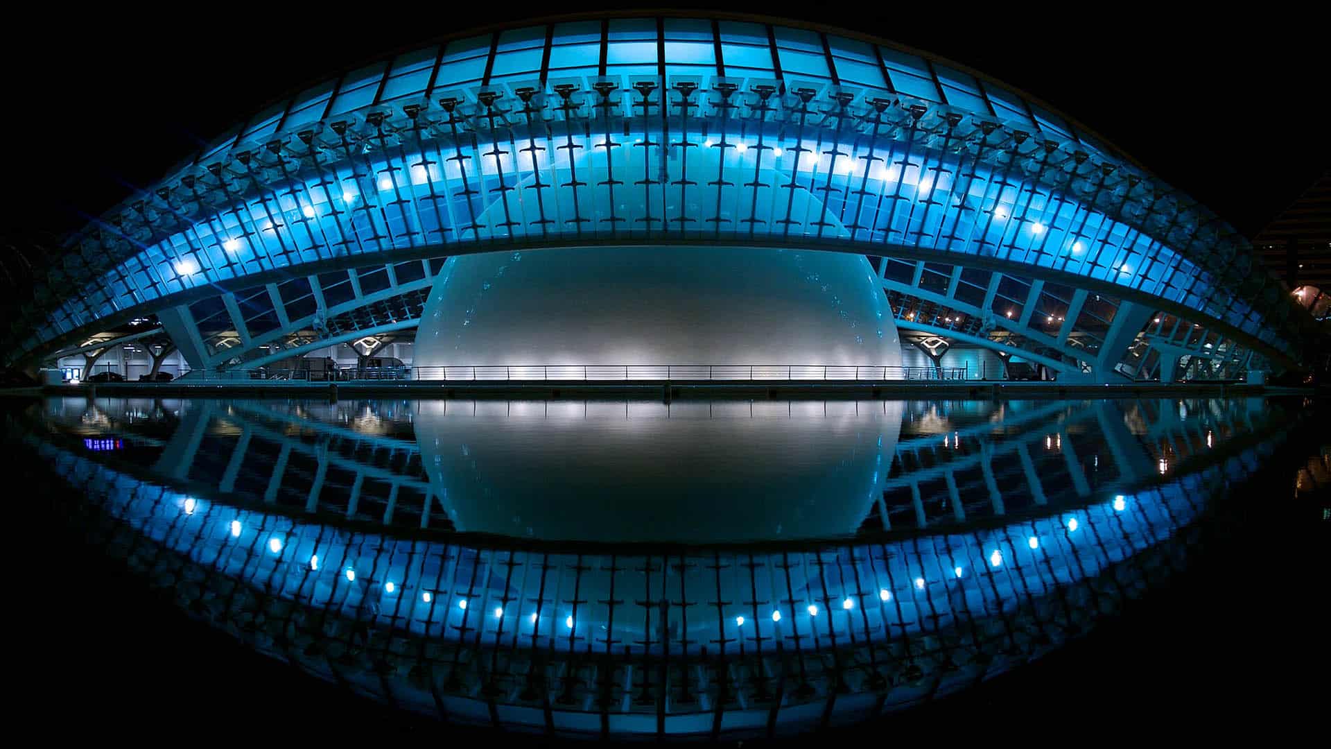 Foto del edificio L’Hemisferic, diseñado por Santiago Calatrava con analogía de un ojo, de noche en la Ciudad de las Artes y las Ciencias de Valencia (España). El edificio está iluminado con luces blancas con filtros azules, dando una idea futurista y distópica.