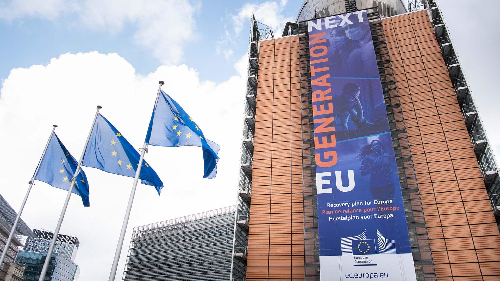 Pancarta del “Plan de Recuperación para Europa” o Next Generation EU en la fachada del edificio Berlaymont, sede de la Comisión Europea en Bruselas, Bélgica. Al lado izquierdo, tres banderas de la UE ondean en sus respectivos mástiles.