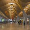 Vestíbulo de la Terminal T4 (Barajas) con techo ondulado de madera, grandes ventanales, paneles de puertas de embarque y viajeros.
