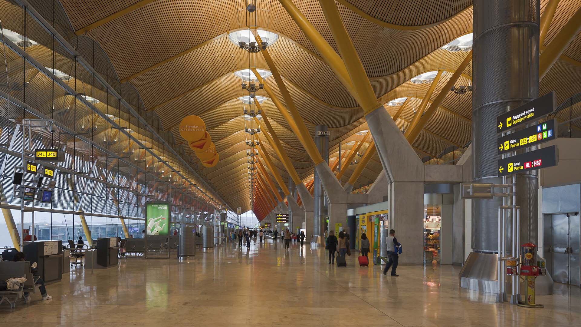 The concourse of Terminal T4 (Barajas) with its undulating wooden ceiling, large windows, boarding gate panels and passengers.