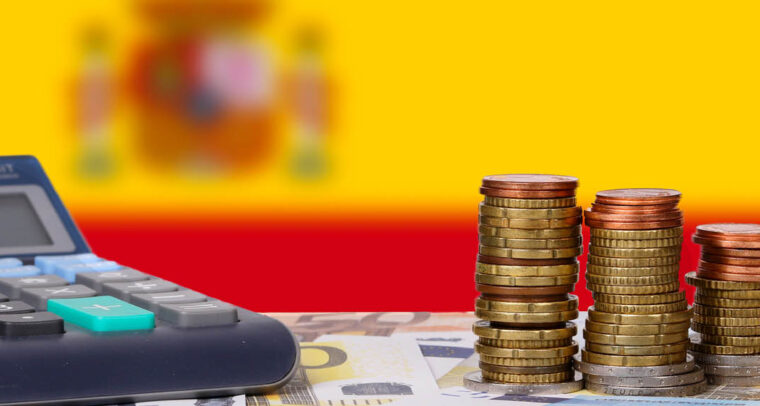 Ups and downs of the Spanish economy. Calculator with money and coins in front of flag of Spain