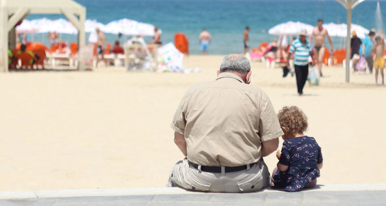 Children. An old man sitting besides a girl on a bench in a beach