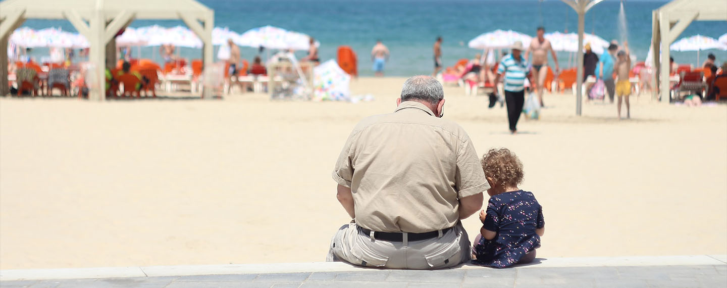 Children. An old man sitting besides a girl on a bench in a beach