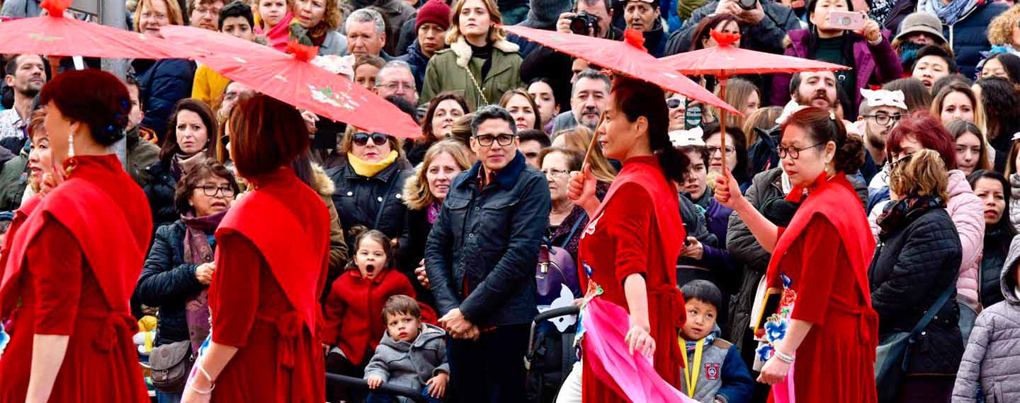 Crowds of people at the Chinese New Year parade in the streets of the Usera neighbourhood, Madrid (Spain). At the front, women dressed in traditional red costumes and umbrellas to welcome the year of the pig
