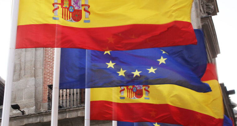 Imagen de las banderas de España y la Unión Europea con la sede del Ministerio de Asuntos Exteriores, de la Unión Europea y Cooperación al fondo