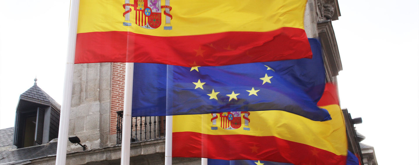 Imagen de las banderas de España y la Unión Europea con la sede del Ministerio de Asuntos Exteriores, de la Unión Europea y Cooperación al fondo