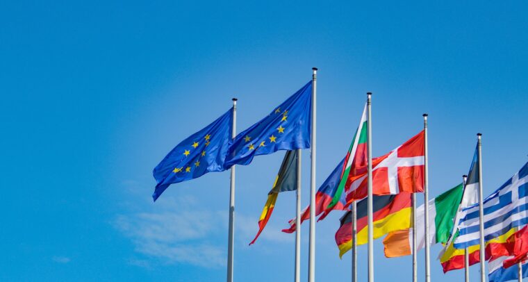 Dos banderas de la Unión Europea al centro acompañadas de banderas de países de Europa ondeando sobre un fondo azul