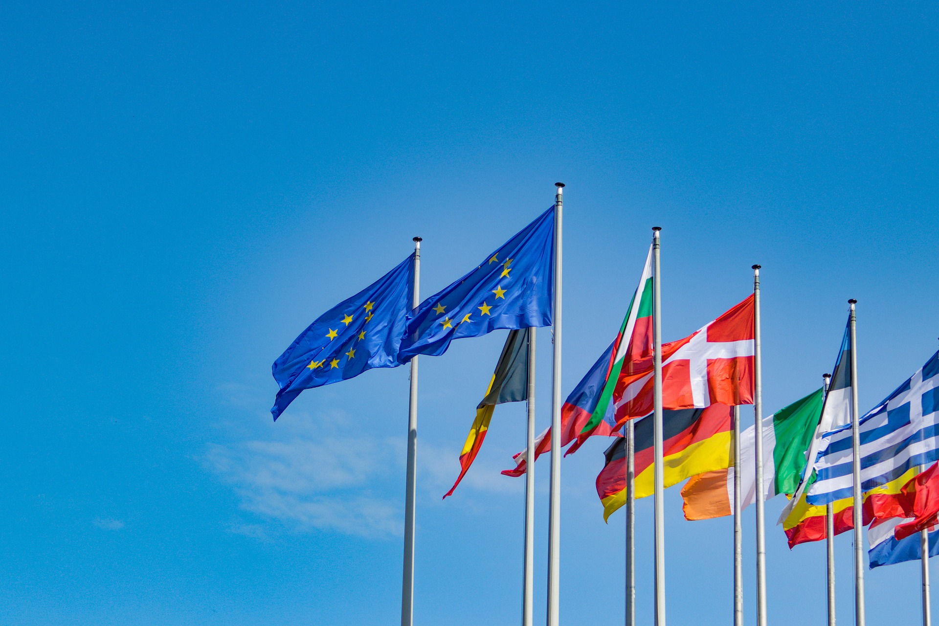 Dos banderas de la Unión Europea al centro acompañadas de banderas de países de Europa ondeando sobre un fondo azul