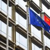 Mastiles con las banderas de la Unión Europea y China frente a un edificio con ventanales en Pekín.