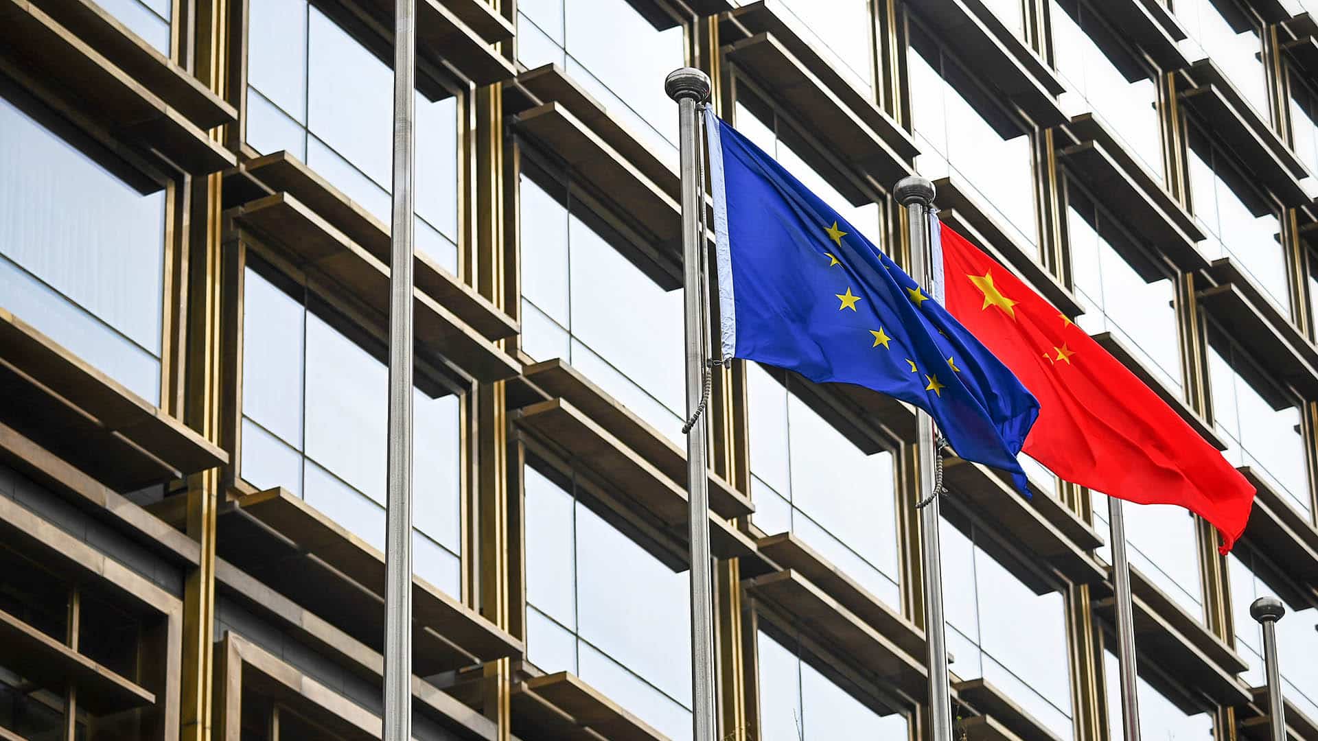 Mastiles con las banderas de la Unión Europea y China frente a un edificio con ventanales en Pekín.