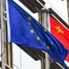 Mastiles con las banderas de la Unión Europea y China frente a un edificio con ventanales en Pekín