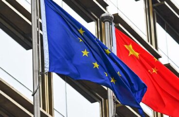 Mastiles con las banderas de la Unión Europea y China frente a un edificio con ventanales en Pekín