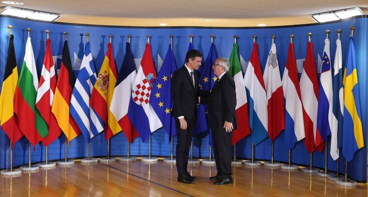 Pedro Sánchez (presidente del Gobierno de España) y Jean-Claude Juncker (presidente de la Comisión Europea) en la recepción de una reunión informal sobre asuntos de migración y asilo en Bruselas, Bélgica. Al fondo las banderas de los Estados miembros de la UE (24/06/2018).