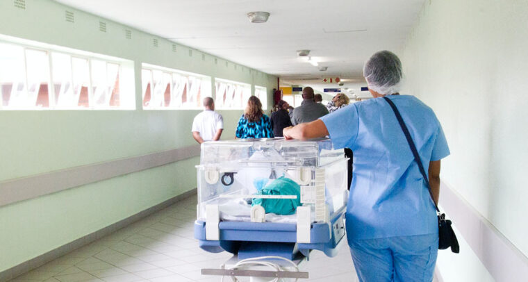 Personal de enfermería caminando por el pasillo de un hospital al lado de una incubadora con un bebé. Salud global