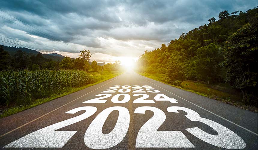 Texto año 2023, 2024, 2025 escrito en medio de una carretera de asfalto con el atardecer al fondo, en un paisaje rural y boscoso. Concepto de planificación, meta, desafío, resolución de año nuevo