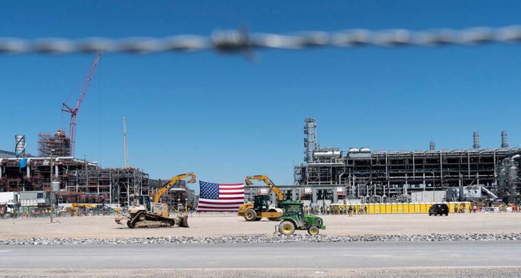 Foto tomada a través de una alambrada de la terminal de exportación en la planta de licuefacción de gas natural licuado Cameron en Hackberry, Louisiana (EEUU). En el centro se observa una bandera estadounidense gigantesca en medio de dos maquinarias de palas de construcción
