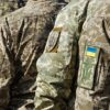 Brazos de soldados de las Fuerzas Armadas ucranianas, con las banderas y escudos de Ucrania en sus insignias, en un desfile militar