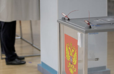 A la izquierda, personas de pies en las cabinas y a la derecha, unas urnas electorales con el escudo de la Federación Rusa en un colegio electoral durante las pasadas elecciones legislativas de 2021
