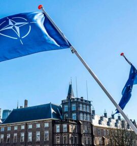 Banderas de la OTAN ondeando en La Haya, Países Bajos. Fondo: Ciudad de La Haya de día, con el cielo azul.