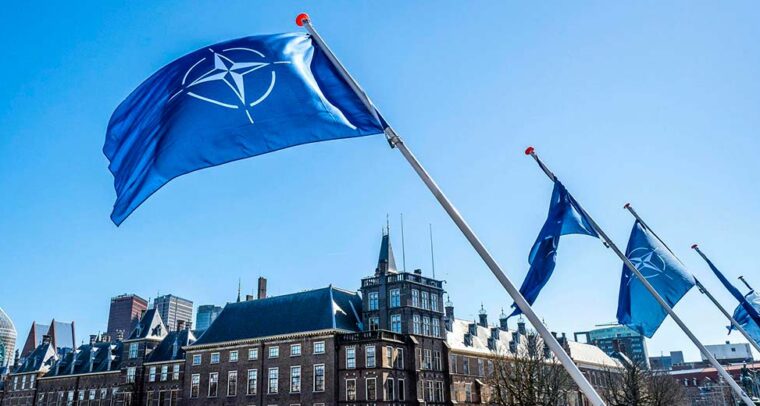 Banderas de la OTAN ondeando en La Haya, Países Bajos. Fondo: Ciudad de La Haya de día, con el cielo azul.