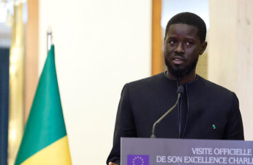 El nuevo presidente de Senegal, Bassirou Diomaye Faye, durante la rueda de prensa con motivo de la visita de Charles Michel, presidente del Consejo Europeo, en Dakar. Fondo: Banderas de Senegal y de la Unión Europea.