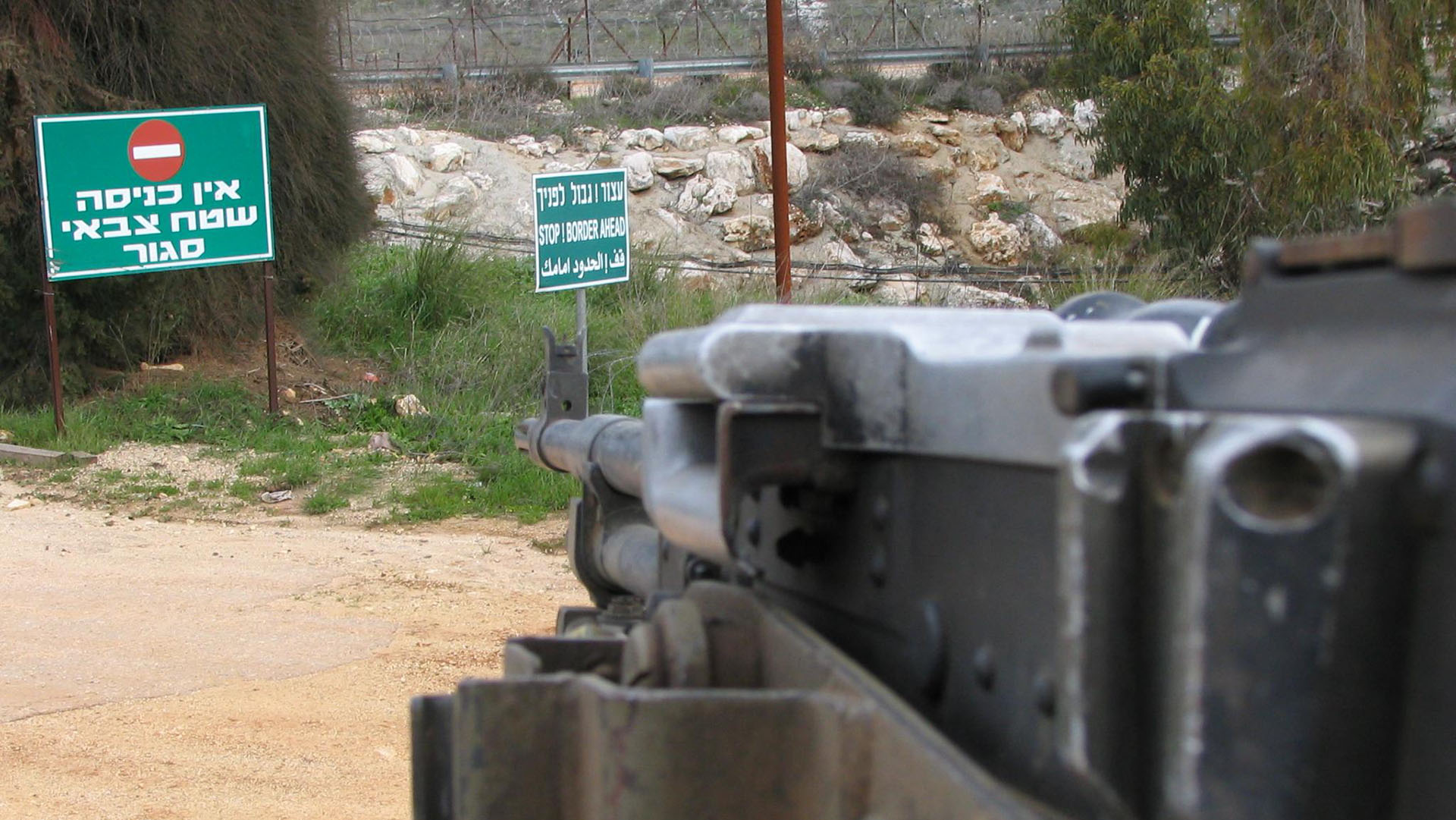 Frontera de Israel y Líbano. Foto tomada desde un carromato militar. En la carretera, unos carteles en verde con letras blancas (y la señal de stop) en hebreo que dicen “Prohibida la entrada, zona militar cerrada”, y en inglés “Alto, frontera adelante”