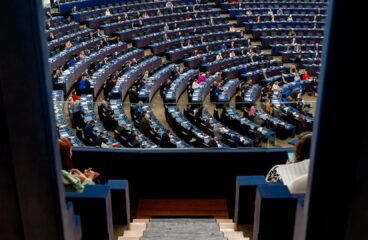 Vista del hemiciclo del Parlamento Europeo con los parlamentarios sentados en sesión. La foto fue tomada desde la puerta en lo alto de una escalera pequeña en una cabina lateral con cristales.