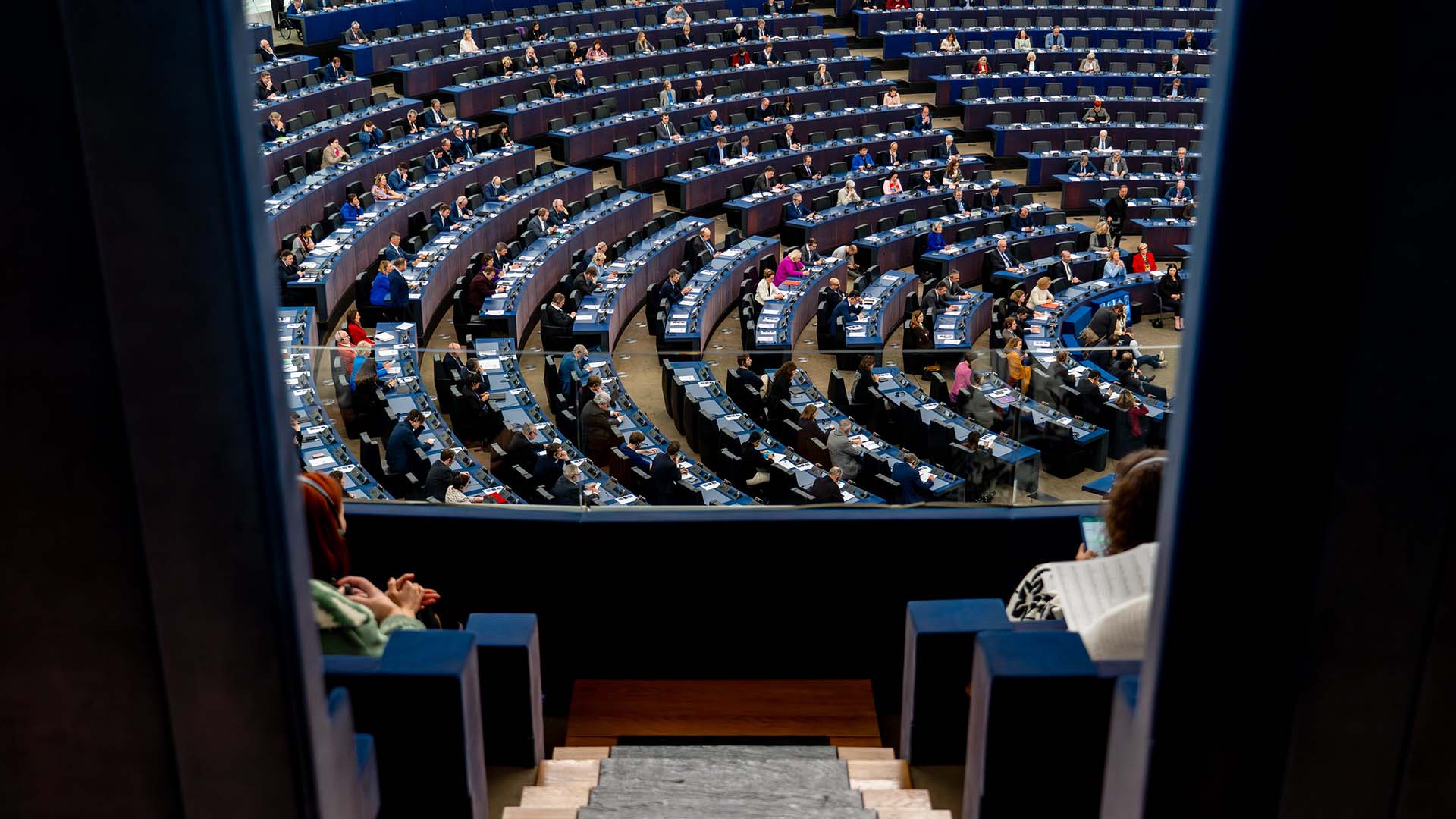 Vista del hemiciclo del Parlamento Europeo con los parlamentarios sentados en sesión. La foto fue tomada desde la puerta en lo alto de una escalera pequeña en una cabina lateral con cristales.