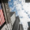 Foto tomada en picado hacia el cielo del edificio de la Bolsa de Nueva York, con una bandera estadounidense gigante en su fachada. política económica de euu