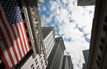 Foto tomada en picado hacia el cielo del edificio de la Bolsa de Nueva York, con una bandera estadounidense gigante en su fachada. política económica de euu