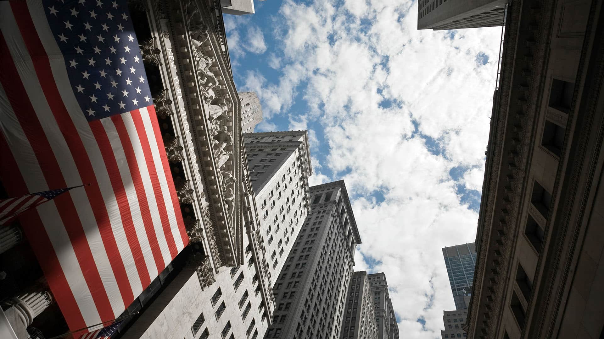 Foto tomada en picado hacia el cielo del edificio de la Bolsa de Nueva York, con una bandera estadounidense gigante en su fachada. política económica de euu