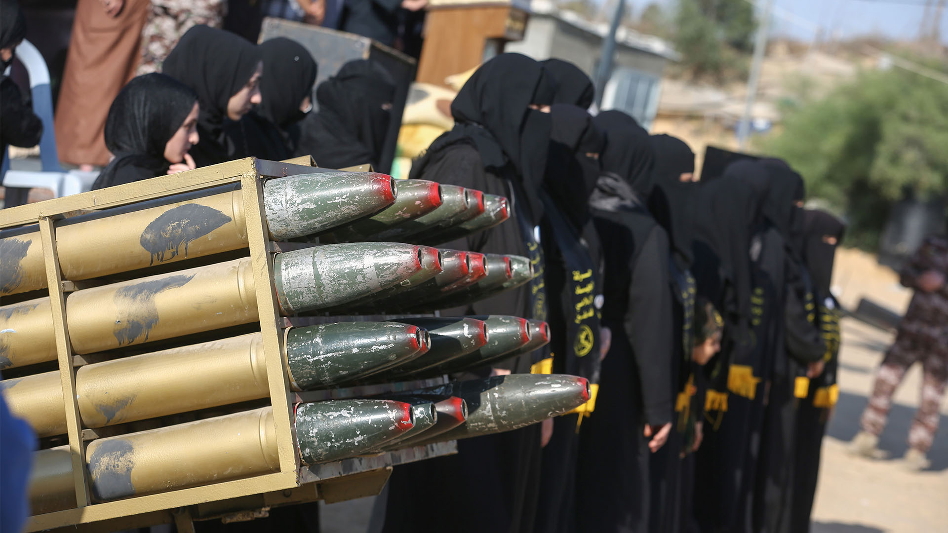 Grupo de mujeres vestidas de negro, con el rostro cubierto, asisten a un campamento militar de verano para jóvenes, organizado por las Brigadas Al-Quds, el ala militar del Movimiento de la Yihad Islámica, dentro de uno de sus emplazamientos militares en la ciudad de Khan Yunis. En primer plano, se aprecian unos proyectiles