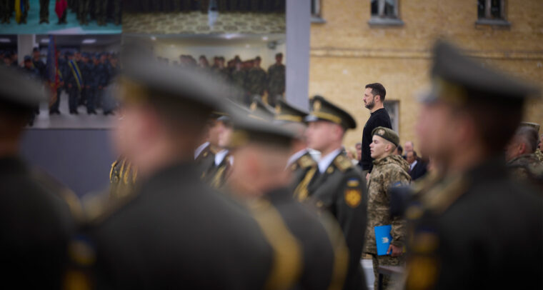 Acto del Día de los Defensores de Ucrania, el 1 de octubre de 2024. En primer plano difuminado, soldados y oficiales ucranianos están formados durante el evento. De fondo, el presidente de Ucrania, Volodímir Zelenski, participando en la ceremonia de homenaje. Ucrania ante sus límites