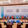 Plenario de la reunión de la Organización de Cooperación de Shanghái (OCS) en Samarcanda (Uzbekistán), en septiembre de 2022, con la participación de líderes de los Estados miembros sentados en una mesa redonda. Al fondo un panel de la reunión en los idiomas oficiales y las banderas con sus mástiles de los distintos países pertenencientes a la OCS