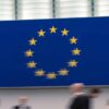 Session at the European Parliament, with the European Union logo in the background and blurred human figures in motion. Deepening for widening