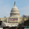 Frontal del edificio del Capitolio de los Estados Unidos, con estatuas y un estanque en primer plano, y banderas estadounidenses colgadas en la fachada principal, con la tribuna de juramento para la nueva Presidencia presente.