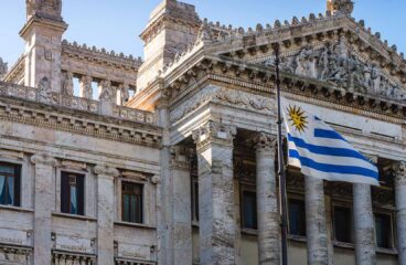 Fachada del Palacio Legislativo de Montevideo, un edificio de estilo neoclásico ubicado en Montevideo, Uruguay, que alberga el Parlamento del país. La imagen muestra una vista frontal del edificio, con una bandera del propio país ondeando delante. Elecciones en Uruguay