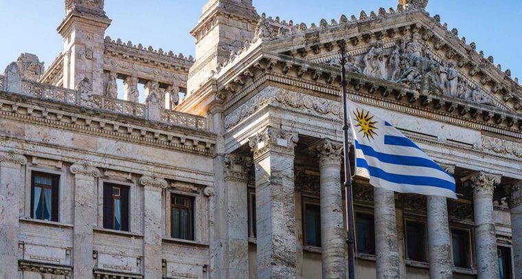 Fachada del Palacio Legislativo de Montevideo, un edificio de estilo neoclásico ubicado en Montevideo, Uruguay, que alberga el Parlamento del país. La imagen muestra una vista frontal del edificio, con una bandera del propio país ondeando delante. Elecciones en Uruguay