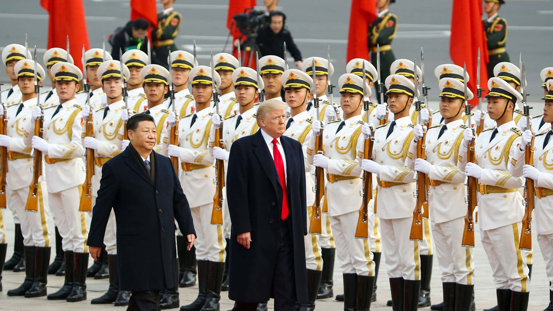 Primer plano de Donald Trump (a la derecha) camina junto a Xi Jinping (izquierda) sobre una alfombra roja en un evento en Pekín, China. En el fondo, una fila de guardias de honor chinos detrás de ellos, sosteniendo rifles. Victoria de trump