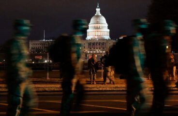 Imagen nocturna del Capitolio de Estados Unidos de noche. En primer plano, un grupo de soldados de la Guardia Nacional patrulla el perímetro. trump