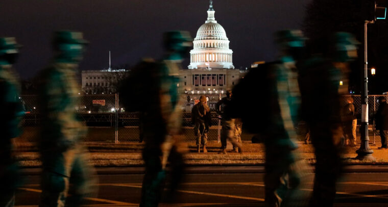 Imagen nocturna del Capitolio de Estados Unidos de noche. En primer plano, un grupo de soldados de la Guardia Nacional patrulla el perímetro. trump