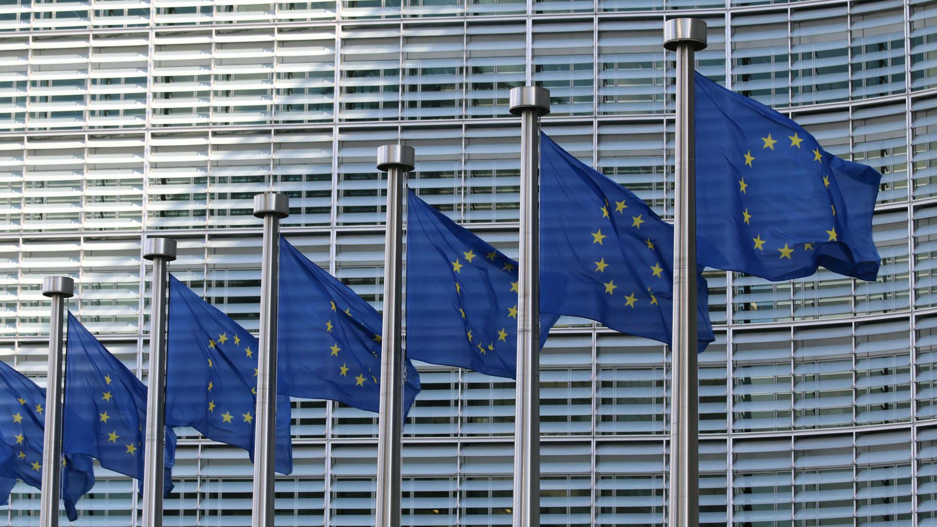 Seven flags of the European Union, with blue background and yellow stars, flying in front of the European Commission headquarters in Brussels (Belgium) during the day. Middle East